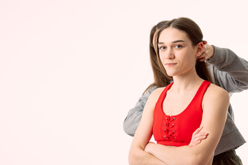Young fit model in red top stands with crossed hands and looking at the camera, her assistant straightens her hair, isolated over white background with copyspace