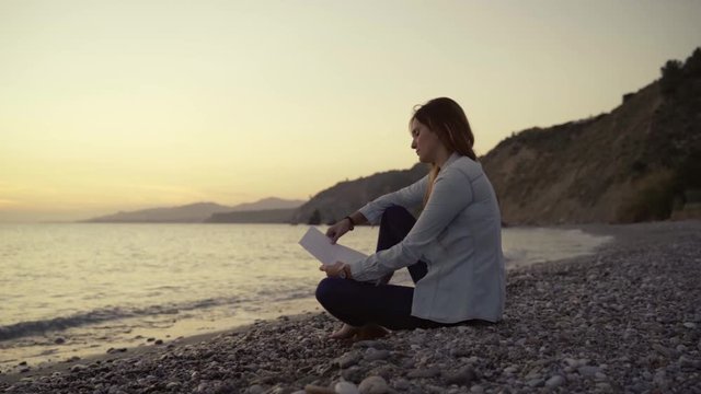 Young woman reading a letter sitting on the beach at sunset