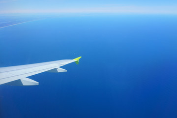 Fototapeta na wymiar Landscape: blue sea, sky, airplane wing. Horizon, coast in the distance. View from the airplane porthole