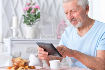 Senior man using tablet while drinking tea at home