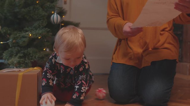 Cute baby boy in sweater playing with Christmas toys sitting with granny on the floor. Family and children. Reunion concept.