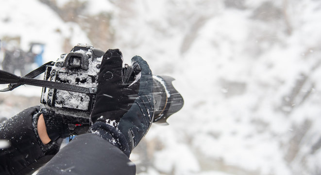 Photographer hands holding camera with snow in winter season.