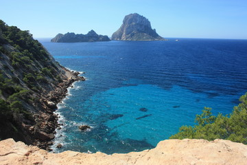 The island of Es Vedra between the blue sky and the blue sea of ​​the Ibizan coasts in front of the Cala D'Hort beach in the Balearic Islands