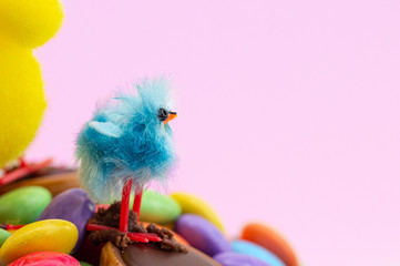 Easter cake chick and colorful chocolate bean decoration on a pink background. Close up of fun kids blue Easter chick. Copy space.