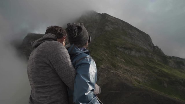 a young, happy couple hugges on a cliff and takes a selfi photo
