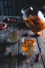 Citrus tea in a transparent teapot and a glass, healthy drink on a wooden background.