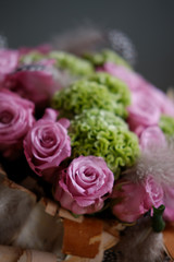 Beautiful spring bouquet close-up with pink roses and green carnations, decorated with feathers and birch bark. 