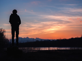A young man in headphones silhouette looks at the sunset
