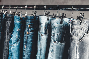 Rack with different jeans on grey background