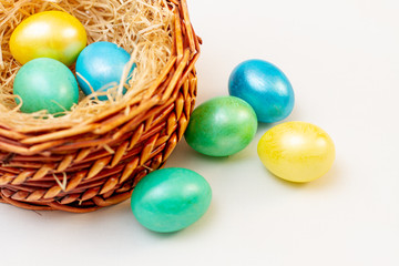multicolored bright easter eggs in a brown basket of twigs on a white background