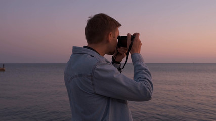 Obraz premium A photographer's man in a denim shirt takes photos of the sea at sunset.
