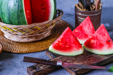 Photo of fresh watermelon with green leaves on wooden board over the table. Whole and sliced....