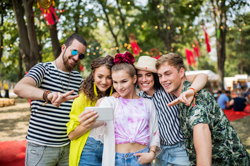 Group of young friends with smartphone at summer festival, taking selfie.