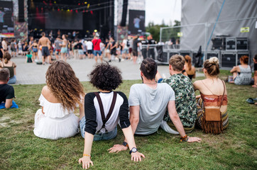 Rear view of group of young friends at summer festival, sitting on ground. - Powered by Adobe