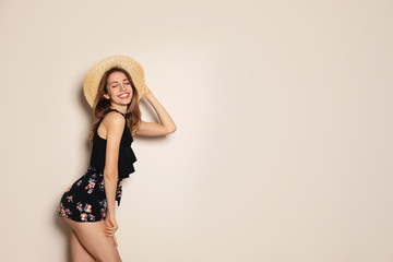 Young woman wearing floral print shorts and straw hat on beige background. Space for text