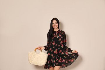 Young woman wearing floral print dress with straw bag on beige background