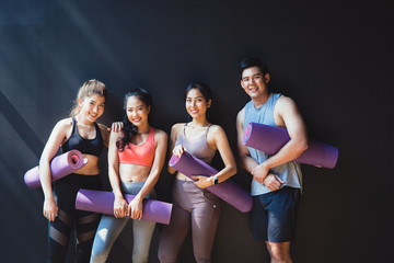 Group of asian young  people with yoga mats standing at Black wall. They smile happily. They have a good shape. Healthy exercise concept