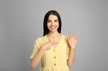 Happy young woman wearing beautiful engagement ring on grey background