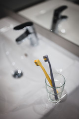 Two toothbrushes in glass cup in bathroom. Yellow and gray toothbrushes. Toothbrushes close up.