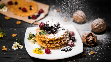 fresh viennese waffles with berries sprinkled with powdered sugar on blackboard on blank background