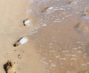 Footprints in the sand washed away by waves at beach
