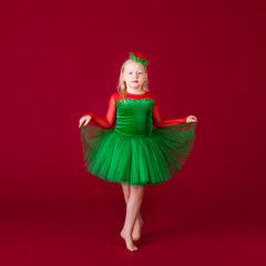 Beautiful little plump girl princess dancing in luxury green dress isolated on red background. Carnival party with costumes
