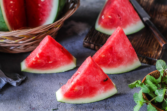 Photo of fresh watermelon with green leaves on wooden board over the table. Whole and sliced. Cutting board. Cut in halves. Dark background. Front view. Raw organic fruit. Image