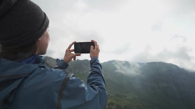 A hiker girl take a pictures on a smartphone in the mountains at sunset