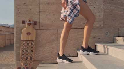 Women's feet in shorts and black sneakers go up the stairs.