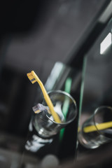 Two toothbrushes in glass cup in bathroom. Yellow and gray toothbrushes. Toothbrushes close up.