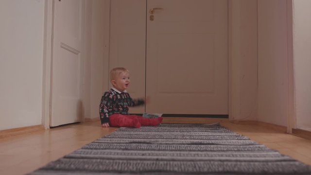 Naughty cute baby boy in holiday Christmas sweater crying with tears playing with paper magazine on floor at home.