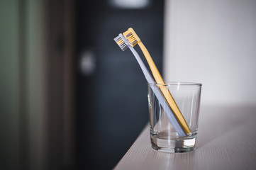 Two toothbrushes in glass cup in bathroom. Yellow and gray toothbrushes. Toothbrushes close up.