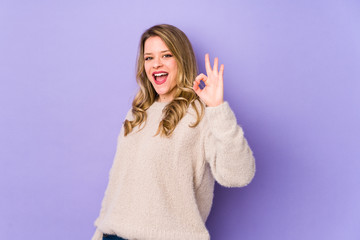 Young caucasian woman isolated on purple background cheerful and confident showing ok gesture.