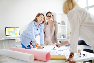 Obraz premium Group of cheerful businesswomen discussing work while collaborating on design project in studio
