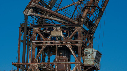 Fototapeta na wymiar A central part of a big old rusty tower crane on the blue sky background