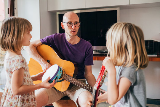 father teaching to his daughters how to play guitar and playing instruments