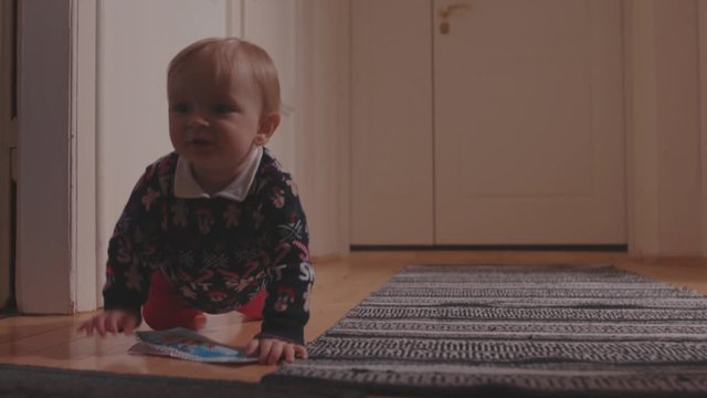 Amazing cute toddler boy wearing xmas sweater crawling on the floor carpet curiously looking around. At home. Concept of childhood.