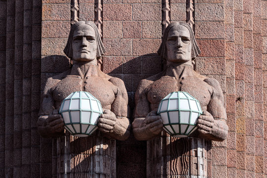 Republic of Finland, Helsinki: Fragment of famous Helsinki Central Station main railway station facade in the Finnish capital with sculptures statues holding spherical art nouveau lamps.
