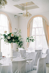 floral decoration of wedding tables, delicate white flowers and branches of fresh greenery on white hall