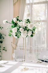 floral decoration of wedding tables, delicate white flowers and branches of fresh greenery on white hall