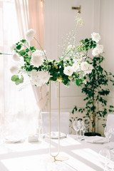 floral decoration of wedding tables, delicate white flowers and branches of fresh greenery on white hall