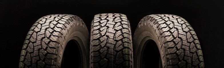 mud all terrain tires for SUVs on a black background close-up, three wheels on a long layout look...
