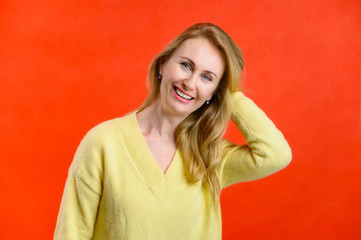 Portrait of a smiling blonde woman 40 years old in a yellow sweater on a red background