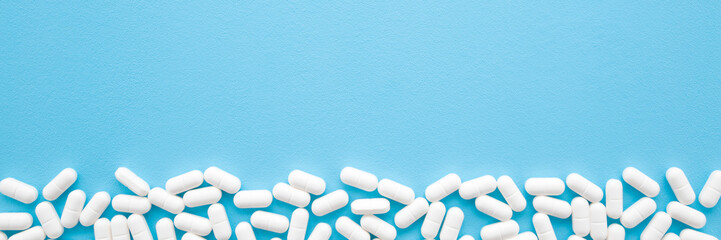 White pills on light pastel blue table. Drugs banner. Medical, pharmacy and healthcare concept. Closeup. Empty place for text or logo. Top down view.