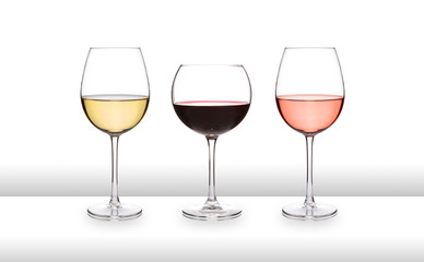 Three glasses of wine, white, red and rose, on a white bar like surface, with a white background and graduated tint