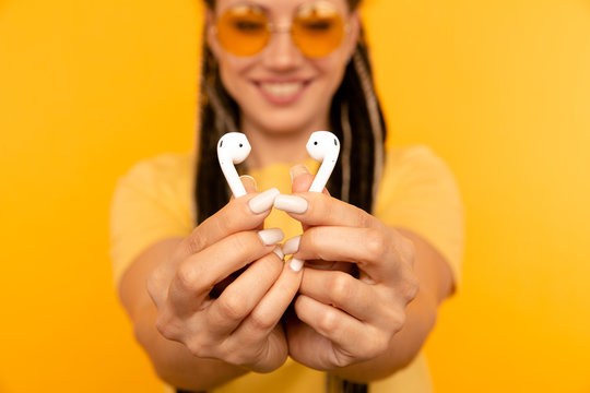 Listening music on airpods. Woman in the yellow studio with white airpods