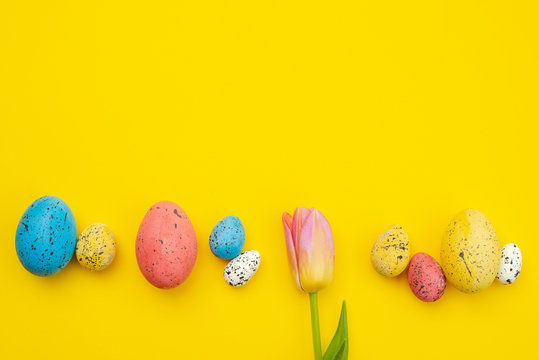 One tulip and colorful eggs .lie on yellow Easter background, copyspace