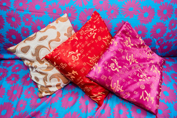Three small size colorful asian pillows laying on a sofa which is blue colored with pink floral patterns