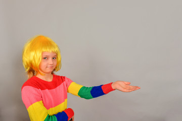 A girl in a yellow wig points to a place for an advertising product, a bright colored child on a gray background.