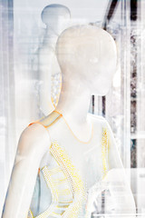 Isolated two white plastic female mannequins wearing elegant wedding dresses behind glass windows, with plenty blurred and reflection effects